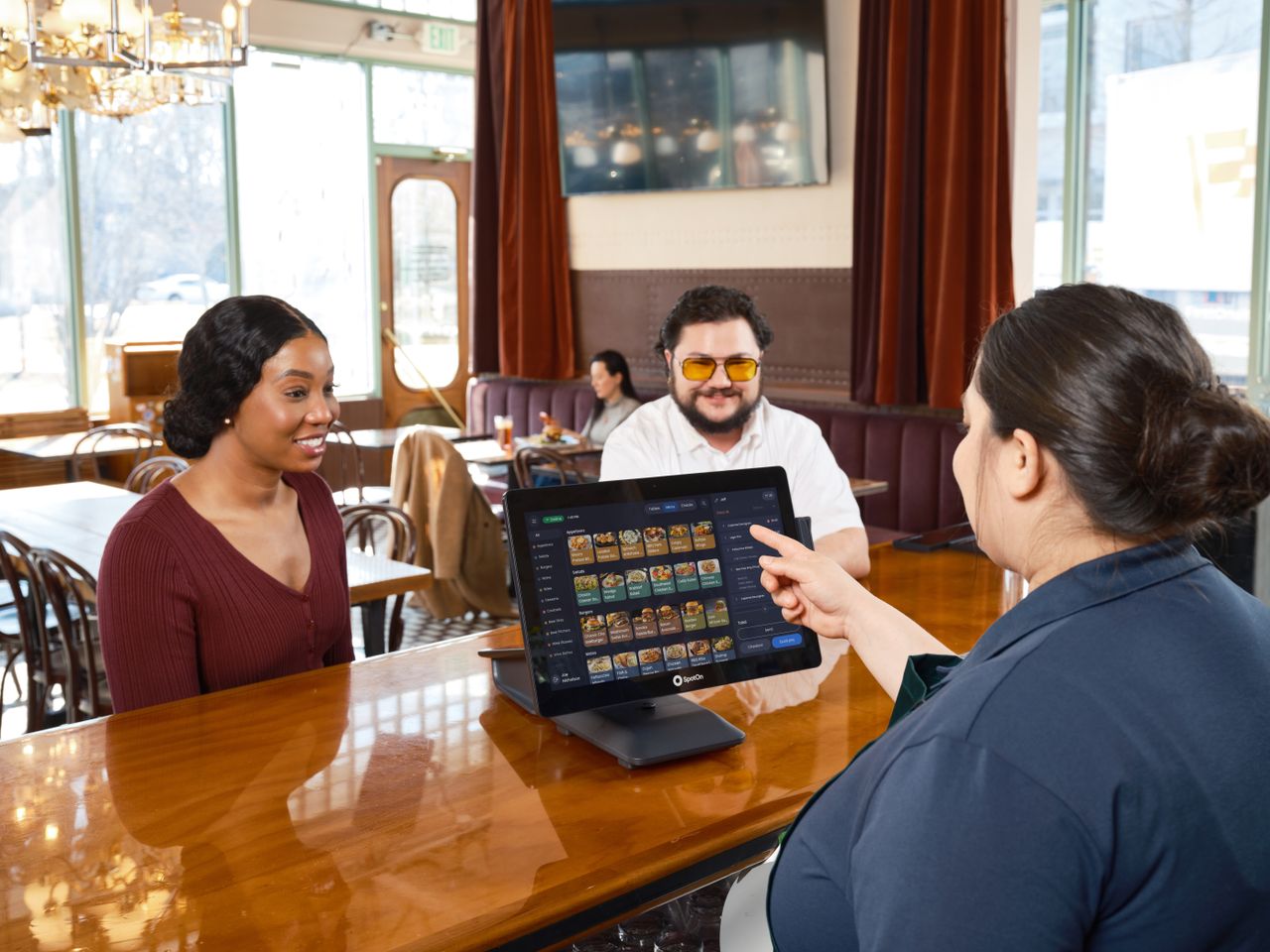 About Server demonstrating a SpotOn POS system for customers in a cozy restaurant setting.