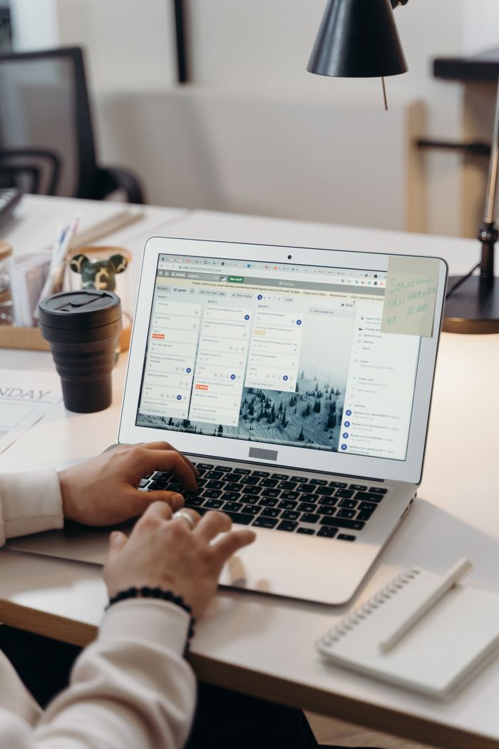 Crafting Captivating Headlines: Your awesome post title goes here Hands typing on a laptop in a modern office setting with notes and task management software visible on the screen.